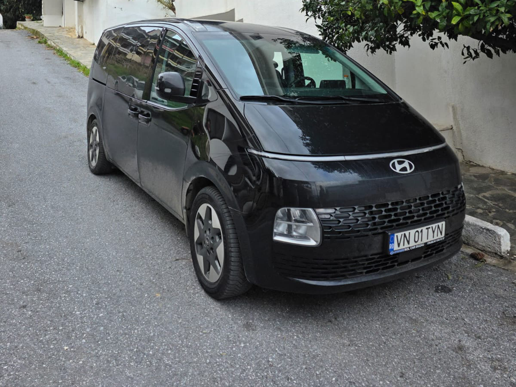 Hyundai Staria neagră parcată pe o stradă îngustă, între case văruite în alb
